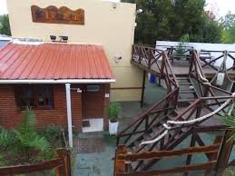 Exterior de la posada, con acceso de piedra, plantas y techo de chapa rojo.